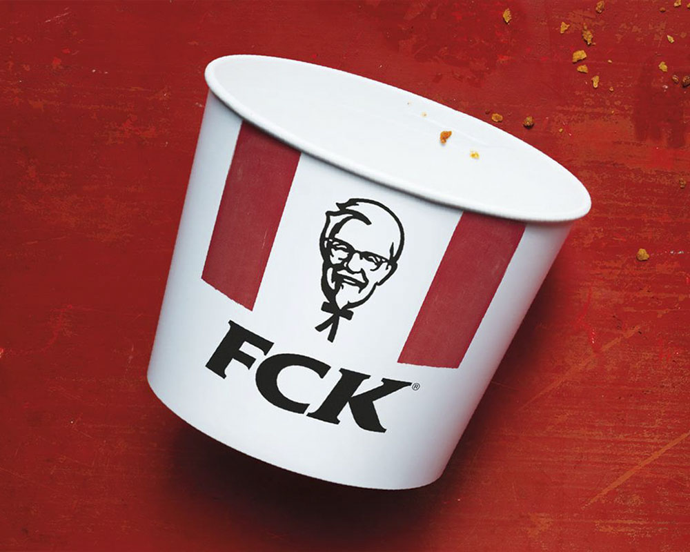 Cartel publicitario rojo con un cubo de pollo frito vacío donde las siglas de KFC han sido alteradas para formar la palabra FCK.