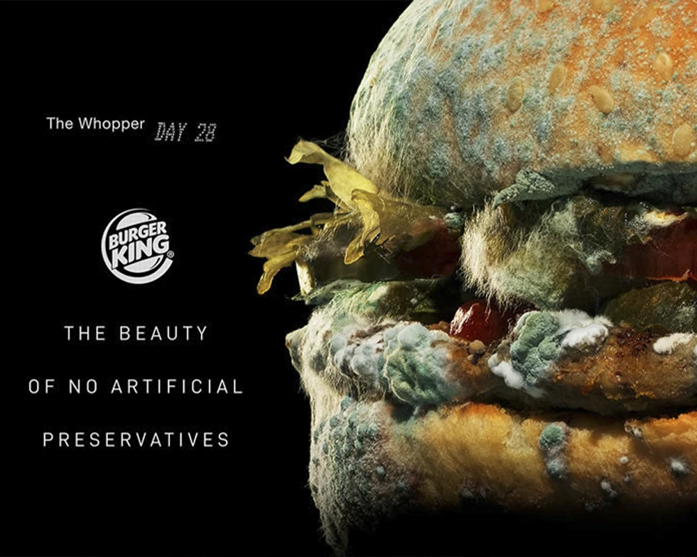 Fotografía publicitaria de una hamburguesa Whopper de Burger King en avanzado estado de descomposición y cubierta de moho sobre un fondo negro.