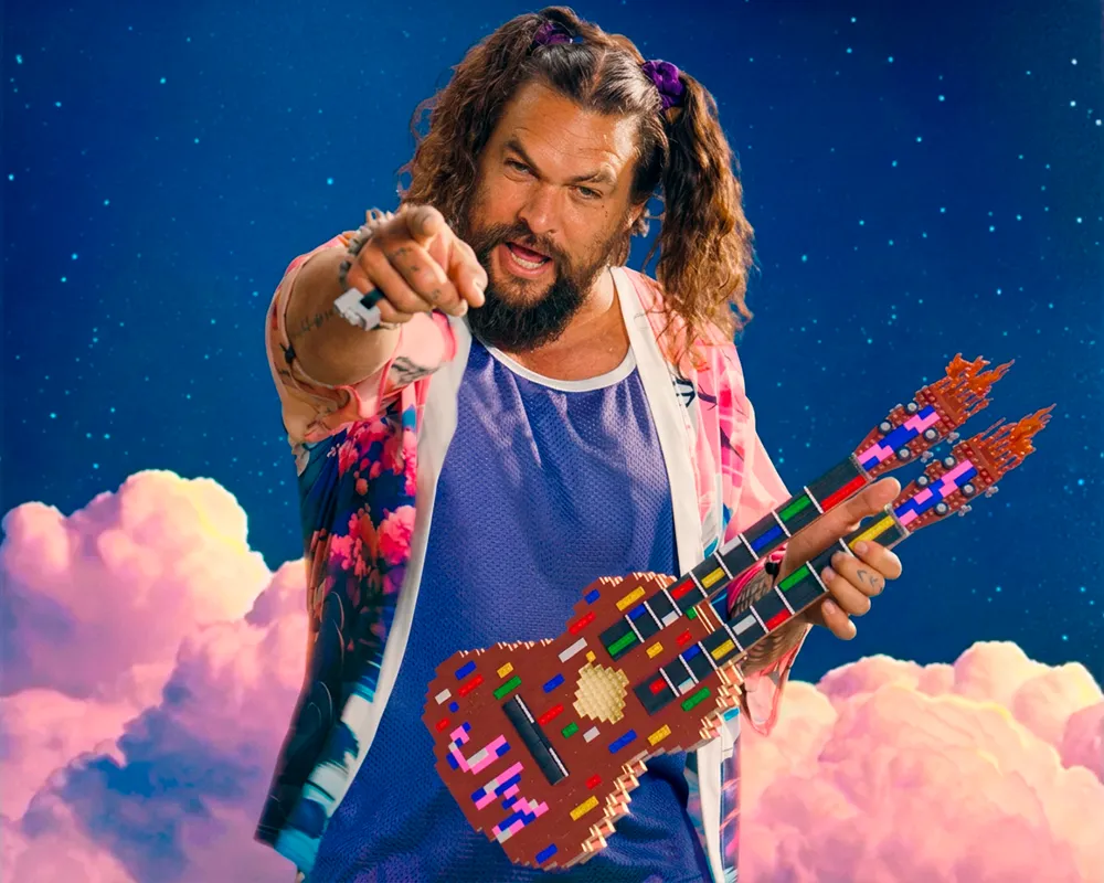 El actor Jason Momoa irrumpiendo con actitud caótica en una sala de juntas corporativa durante la campaña World Play Day de LEGO.