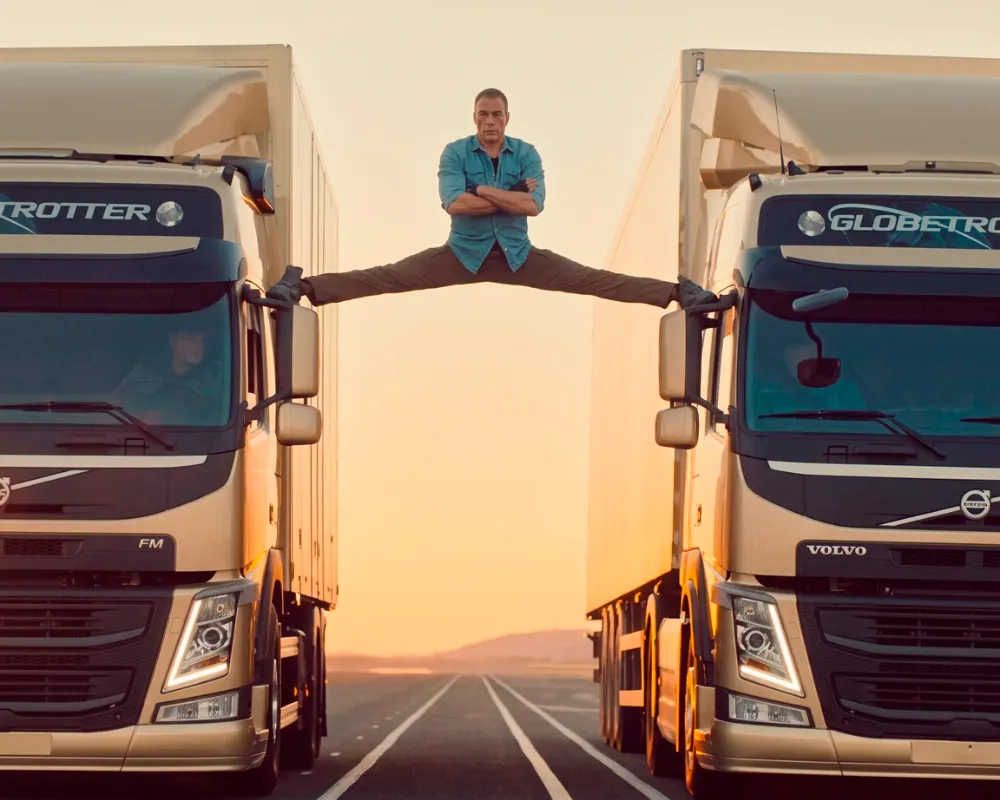 Jean-Claude Van Damme realizando una apertura de piernas apoyado sobre los retrovisores de dos camiones Volvo que circulan marcha atrás.